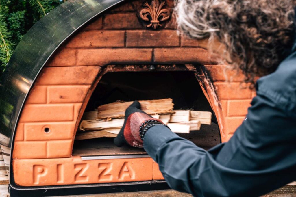Dokładanie drewna do opalanego drewnem pieca do pizzy Pizza Party podczas rozgrzewania pieca.