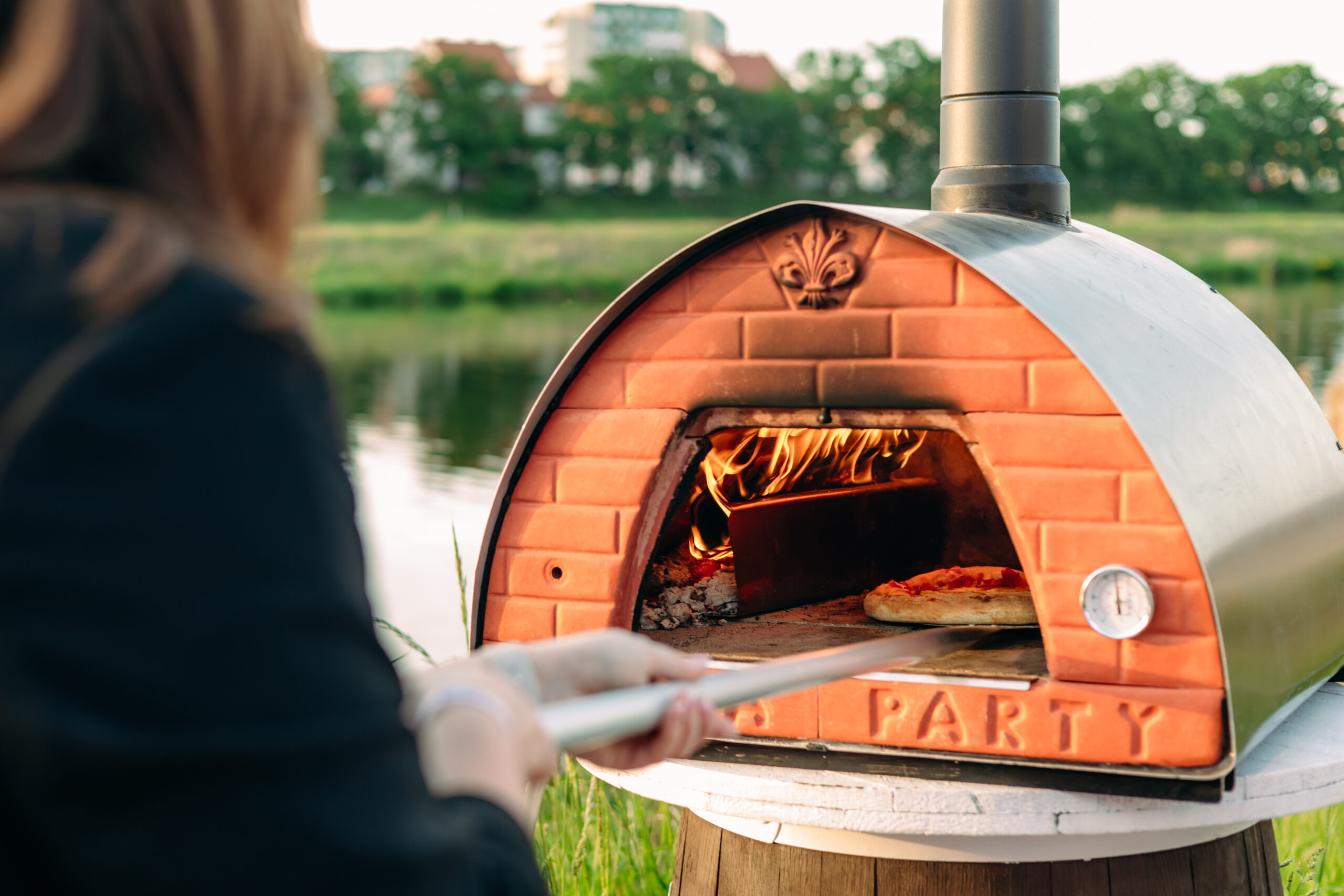 Osoba wkładające pizzę do pieca opalanego drewnem